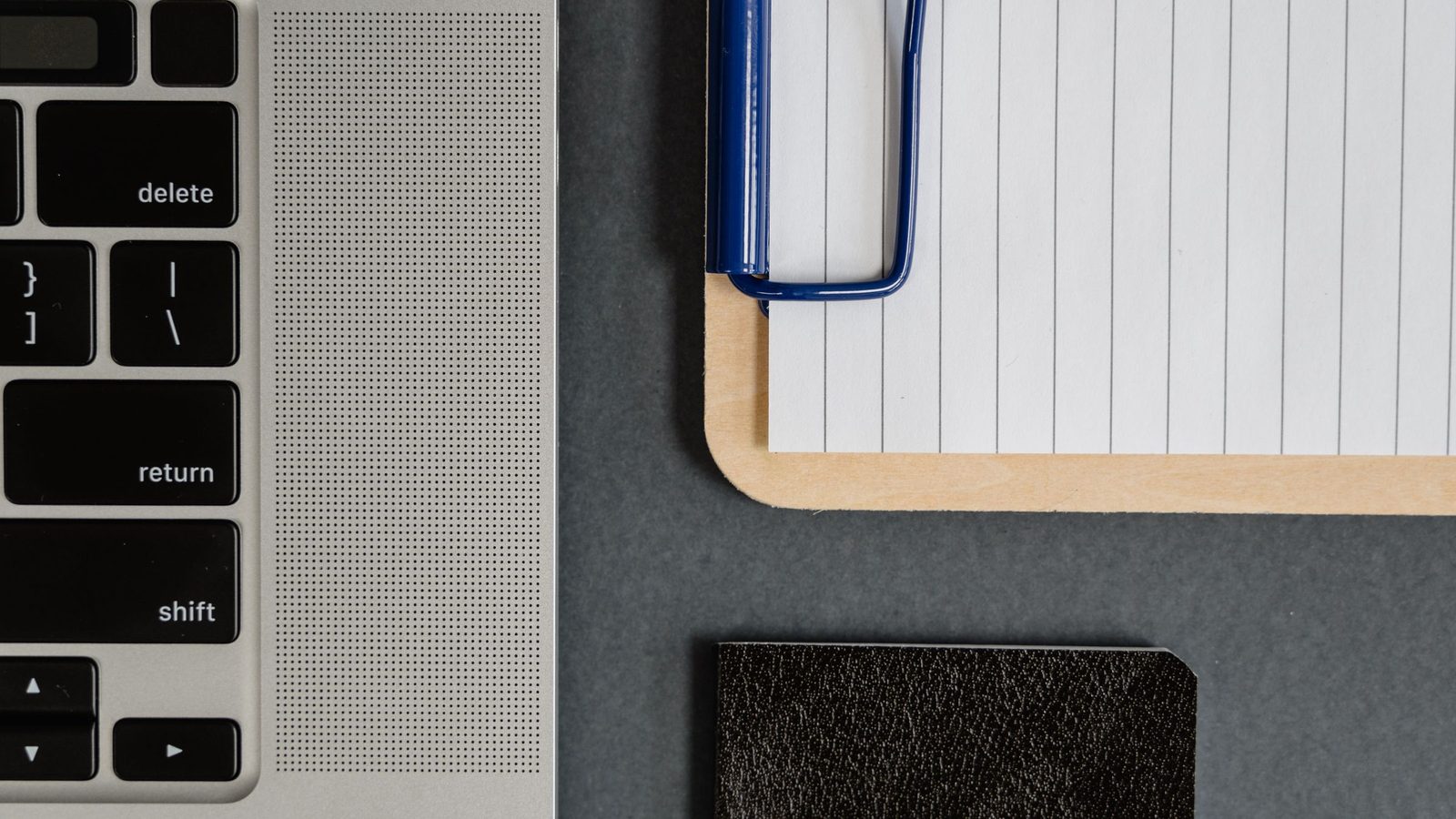 A laptop, a clipboard with lined paper and a notebook on a desk