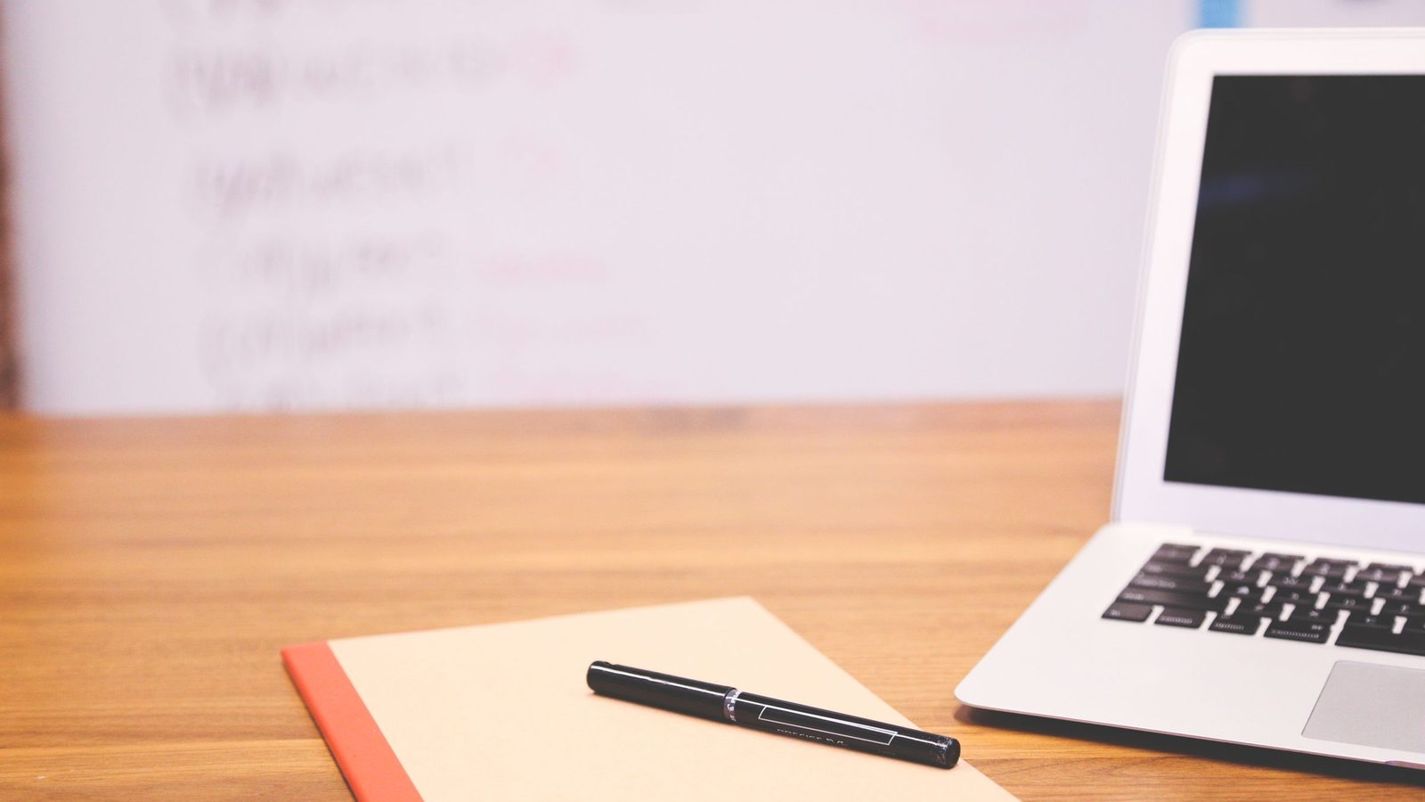 A laptop, an open notebook and a pen on a wooden desk