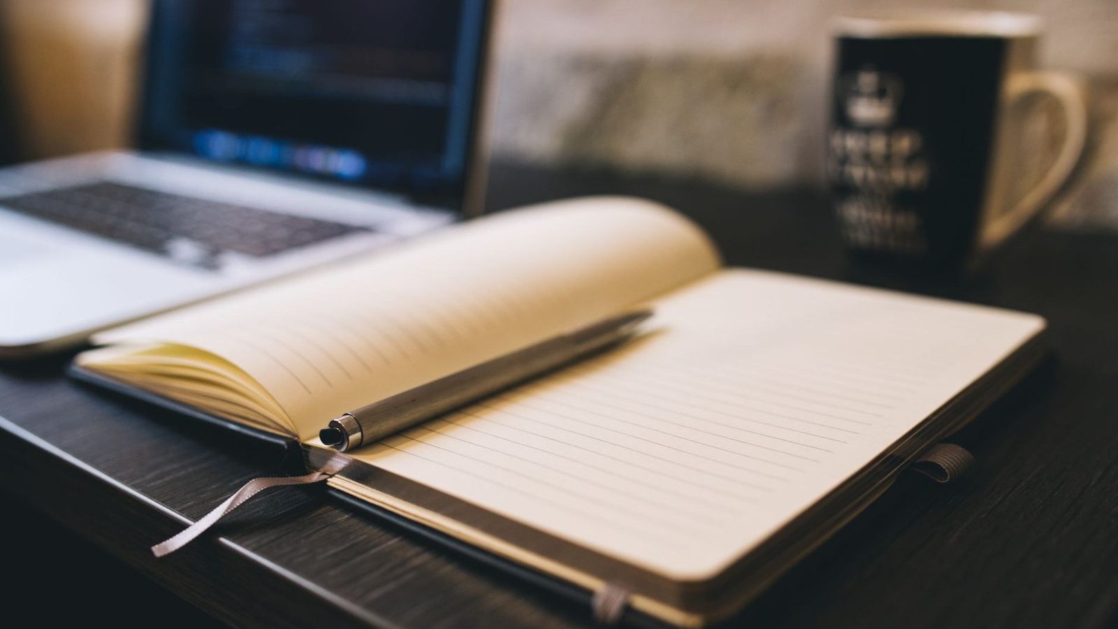 An open notebook and a pen beside a laptop