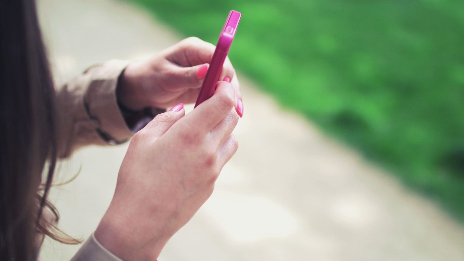 A woman typing a message on a pink smartphone